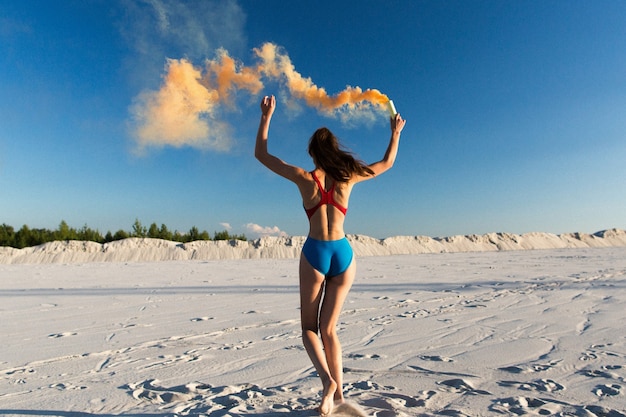 Meisje in blauwe zwemkleding dansen met oranje rook op wit strand