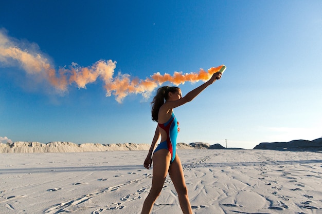 Meisje in blauwe zwemkleding dansen met oranje rook op wit strand