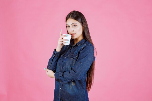 Meisje in denimoverhemd dat een kop van koffie drinkt