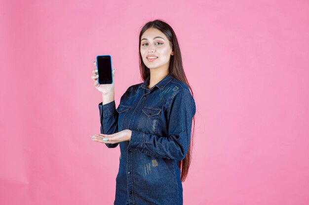 Meisje in denimoverhemd dat haar smartphone toont en duim opmaakt