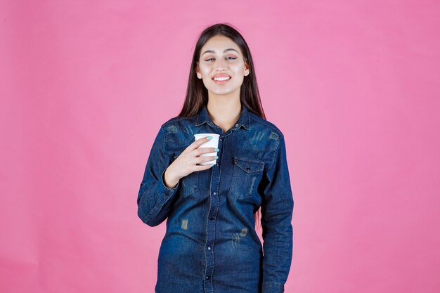 Meisje in denimoverhemd met een koffiekopje en voelt zich positief