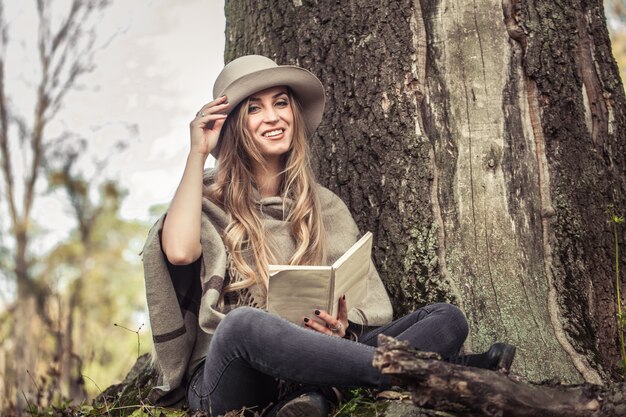 meisje in een hoed die een boek in de herfstbos leest