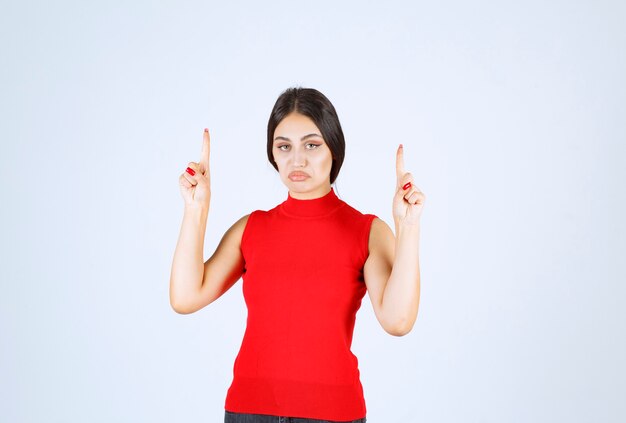 Meisje in een rood shirt dat de hand opsteekt en naar boven wijst.