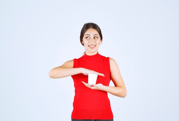 Meisje in een rood shirt met een witte koffiekop tussen handen.