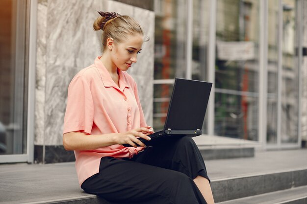 Meisje in een roze shirt zit in de buurt van huis en gebruik de laptop