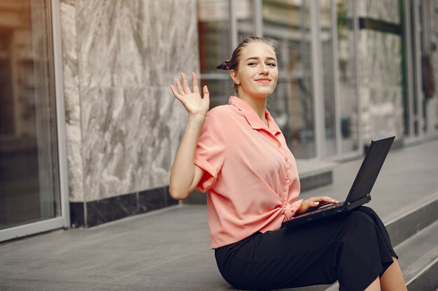 Meisje in een roze shirt zit in de buurt van huis en gebruik de laptop