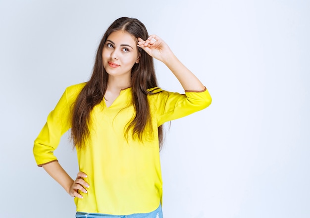 Meisje in geel shirt hand op haar voorhoofd en observeren of op zoek naar iemand.