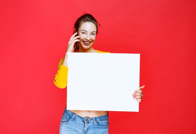 Meisje in geel shirt met een vierkant infobord en praten met de telefoon