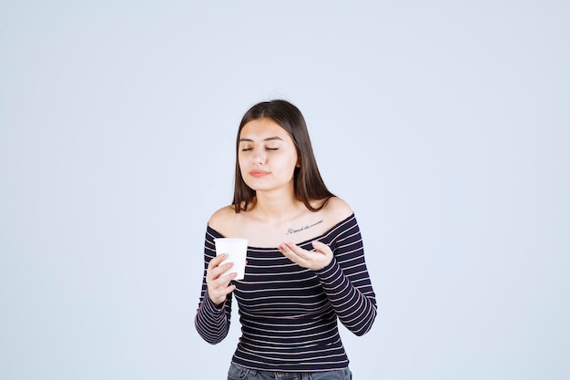 Meisje in gestreept overhemd dat een plastic koffiekop houdt en het ruikt.