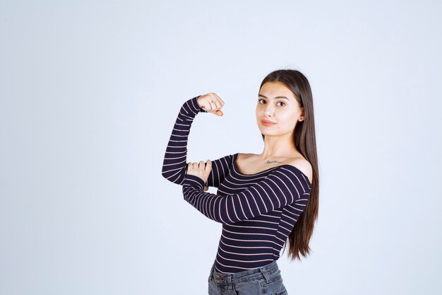 Meisje in gestreept overhemd dat haar armspieren aantoont.