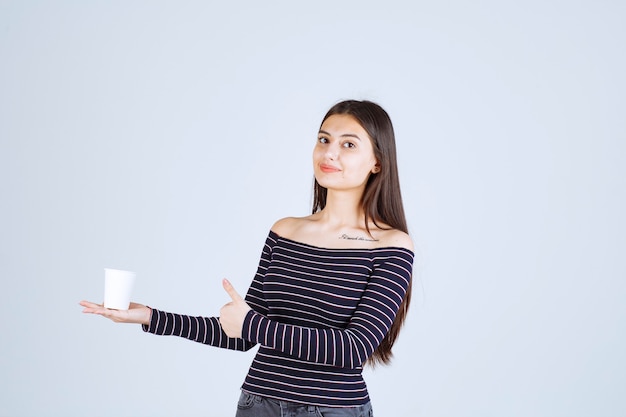 Meisje in gestreept overhemd met een plastic koffiekopje en wijst naar een goede smaak.