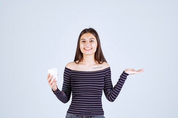 Meisje in gestreept overhemd met een plastic koffiekopje en ziet er positief uit.