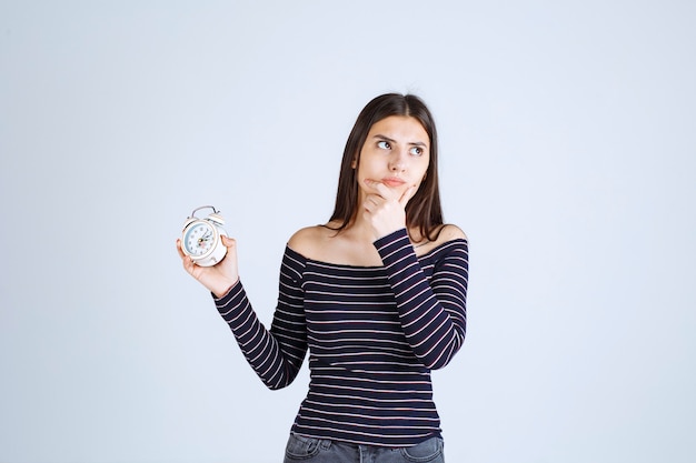 Meisje in gestreept overhemd met een wekker en ziet er doodsbang uit.