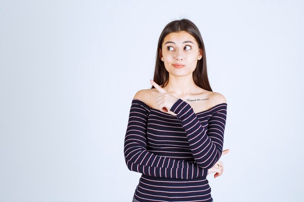 Meisje in gestreept overhemd wijst naar iemand aan de linkerkant.