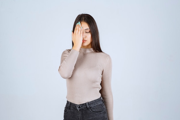 Meisje in grijs overhemd dat haar gezicht met hand sluit.