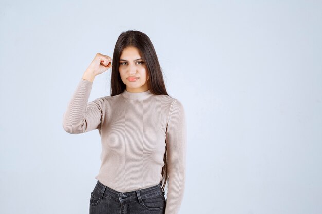 Meisje in grijze sweater die haar vuisten en macht toont.