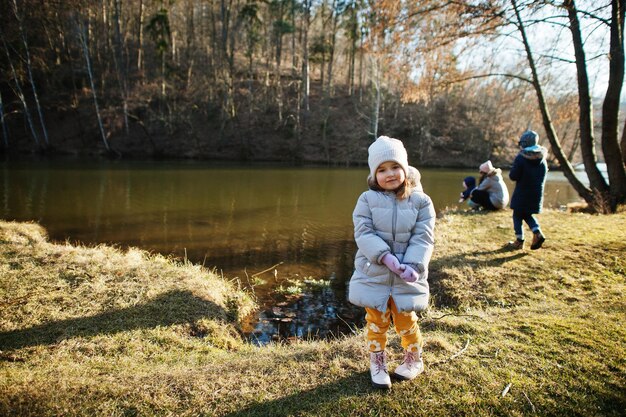 Gratis foto meisje in jasje staat in zonnig lentepark tegen rivier met familie