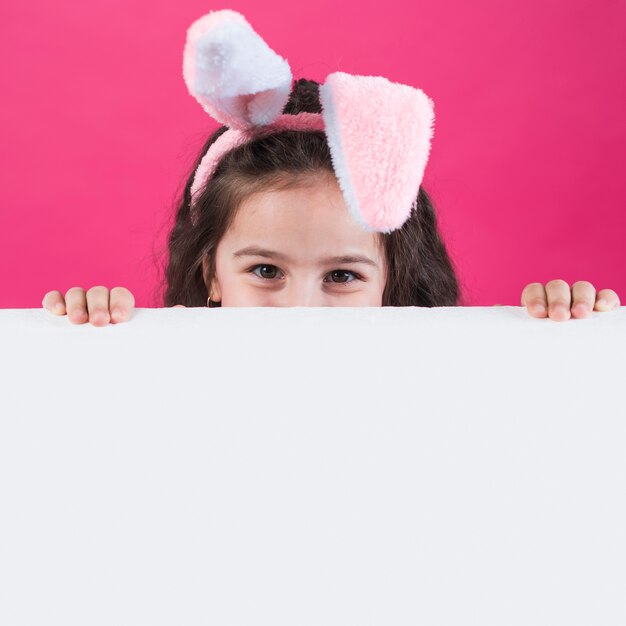 Meisje in konijntjesoren die achter lijst verbergen