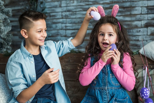 Meisje in konijntjesoren en jongen het spelen met paaseieren