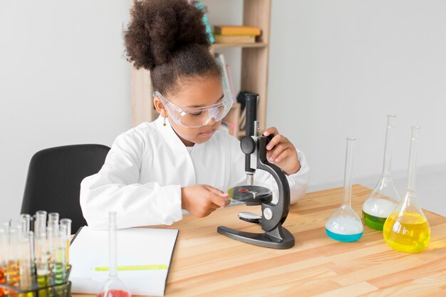 Meisje in laboratoriumjas en veiligheidsbril kijken door de microscoop