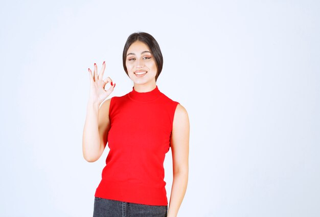 Meisje in rood overhemd dat het teken van de plezierhand toont.