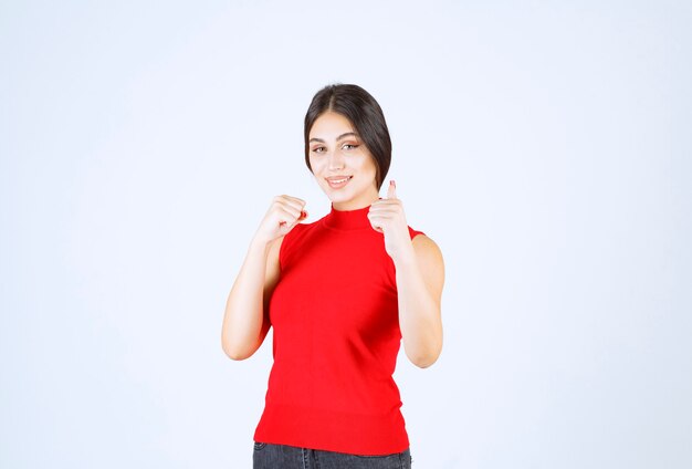 Meisje in rood overhemd dat het teken van de plezierhand toont.