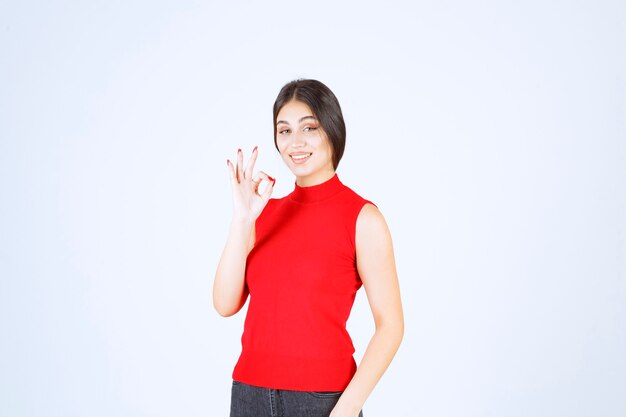 Meisje in rood overhemd dat positief handteken toont.