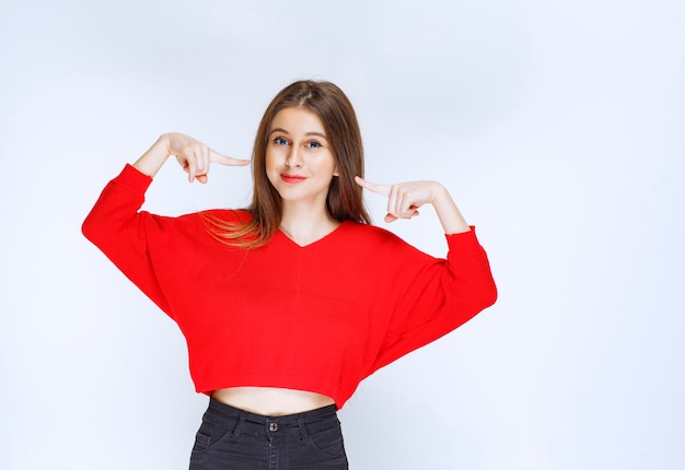 Meisje in rood overhemd wijzend op zichzelf.