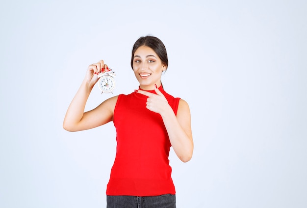 Meisje in rood shirt dat een wekker vasthoudt en promoot.