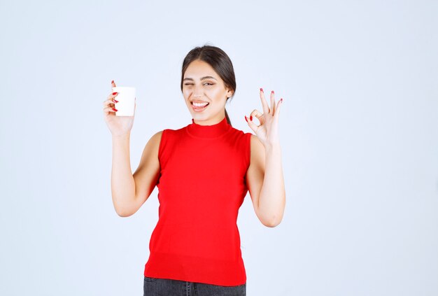 Meisje in rood shirt met koffie en positief teken tonen.