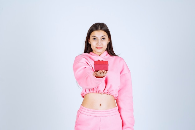 Meisje in roze pyjama houdt een klein rood geschenkdoosje vast en biedt het aan haar vriend aan.