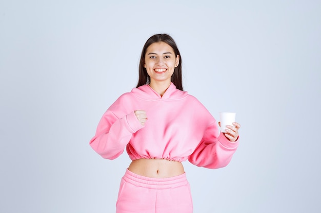 Meisje in roze pyjama's die een koffiekop houden en haar vuist tonen