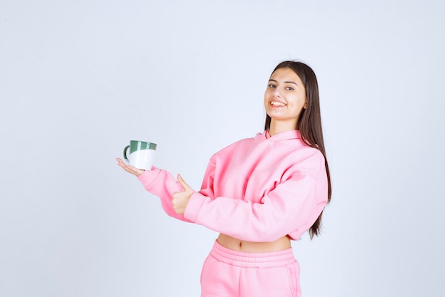 Meisje in roze pyjama's die een koffiemok houden en zich gelukkig voelen.