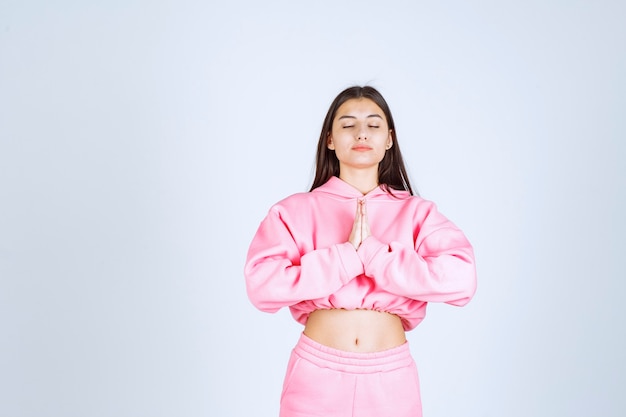 Meisje in roze pyjama's die haar handen verenigen en bidden