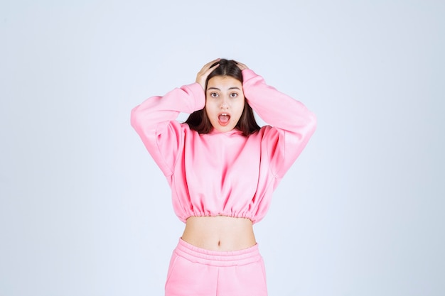 Meisje in roze pyjama's houdt haar hoofd vast als ze uitgeput is of hoofdpijn heeft.