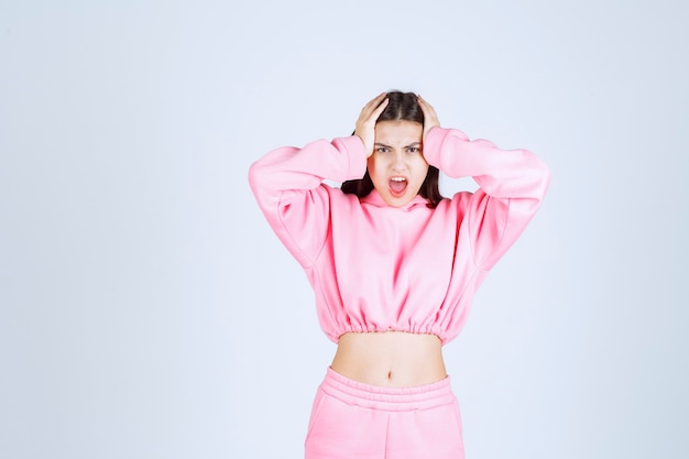 Meisje in roze pyjama's houdt haar hoofd vast als ze uitgeput is of hoofdpijn heeft.