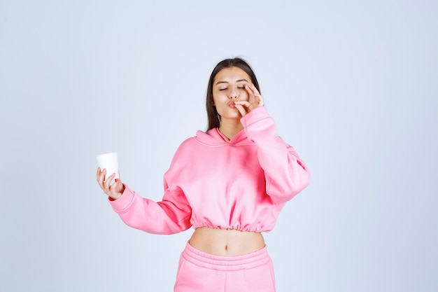 Meisje in roze pyjama's met een koffiekopje en genietend van de smaak