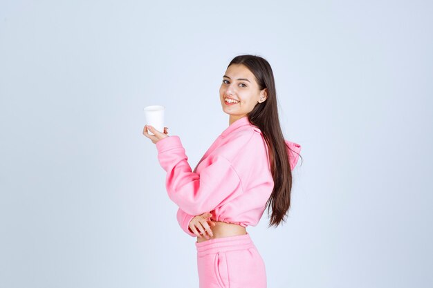 Meisje in roze pyjama's met een koffiekopje en wijzend op iets