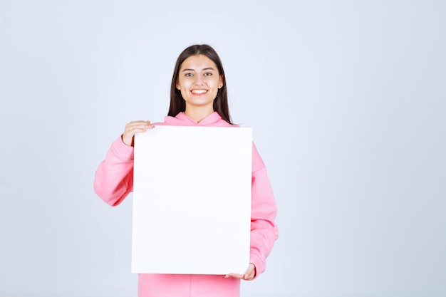 Meisje in roze pyjama's met een leeg vierkant presentatiebord voor haar.