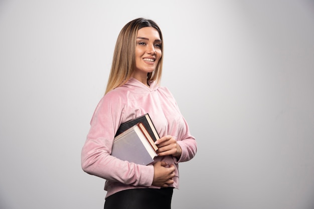 Meisje in roze swaetshirt met een voorraad boeken onder haar arm