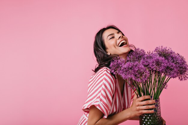 Meisje in roze zomerjurk geniet van de geur van bloemen en lacht oprecht, genietend van een geweldige lentedag.