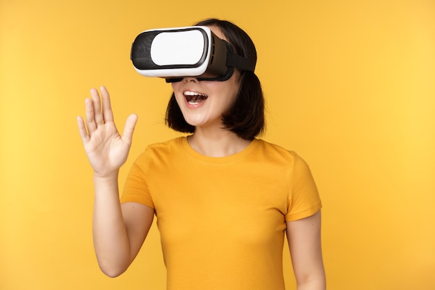 Meisje in VR Mooie jonge aziatische vrouw die een virtual reality-bril gebruikt en aan het chatten is terwijl ze virtueel over gele achtergrond staat