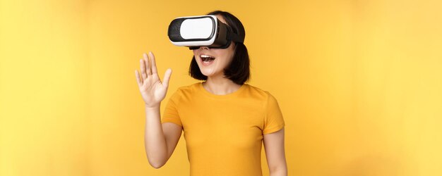 Meisje in VR Mooie jonge aziatische vrouw die een virtual reality-bril gebruikt en aan het chatten is terwijl ze virtueel over gele achtergrond staat