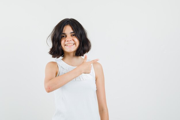 Meisje in witte blouse die naar de kant wijst en vrolijk, vooraanzicht kijkt.