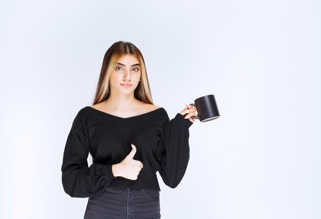 Meisje in zwart shirt met een zwarte koffiemok en genietend van de smaak. Hoge kwaliteit foto