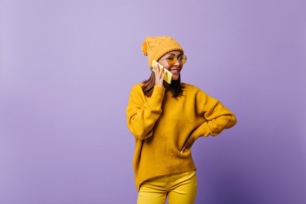 Meisje is dol op oranje kleur en poseren voor nieuwe snapportrait in stijlvolle outfit. Model praten over gele telefoon, vriendelijk lachend