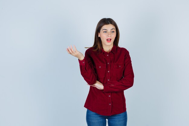 meisje kijkt weg terwijl ze de handpalm opzij spreidt in bordeauxrood shirt en verbaasd kijkt