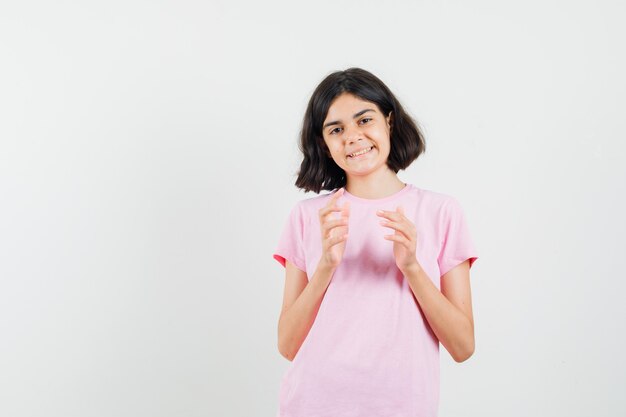 Meisje klaar om te klappen in roze t-shirt en op zoek vrolijk, vooraanzicht.