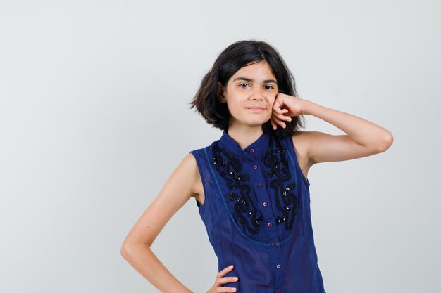 Meisje leunend vuist op wang in blauwe blouse en ziet er prachtig uit