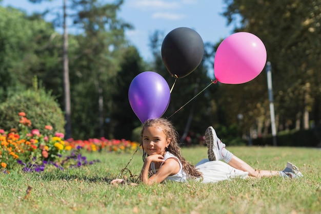 Meisje met ballons die in gras liggen